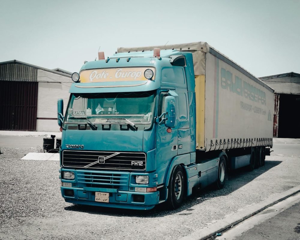 Photo by Esmihel Muhammed https://www.miteco.gob.es/es/calidad-y-evaluacion-ambiental/temas/gestion-de-residuos/residuos-no-peligrosos.aspx - A blue Volvo truck parked outside a warehouse in an industrial area, daytime scene.